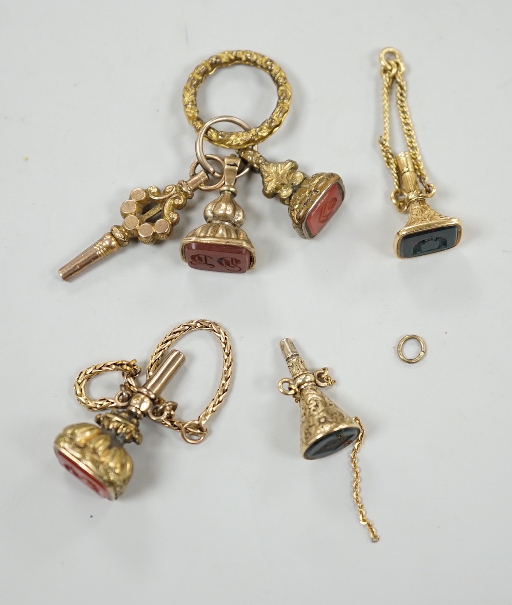 Two 19th century yellow metal overlaid and bloodstone set watch key fobs, one of funnel form, 21mm, a similar gold plated and carnelian set watch key fob, two other fob seals and a watch key on chain.